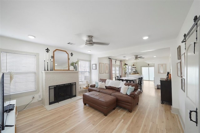 living area with a barn door, light wood-style flooring, a fireplace, visible vents, and a ceiling fan