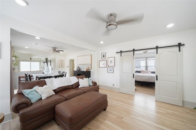 living room with plenty of natural light, ceiling fan, light wood finished floors, and a barn door