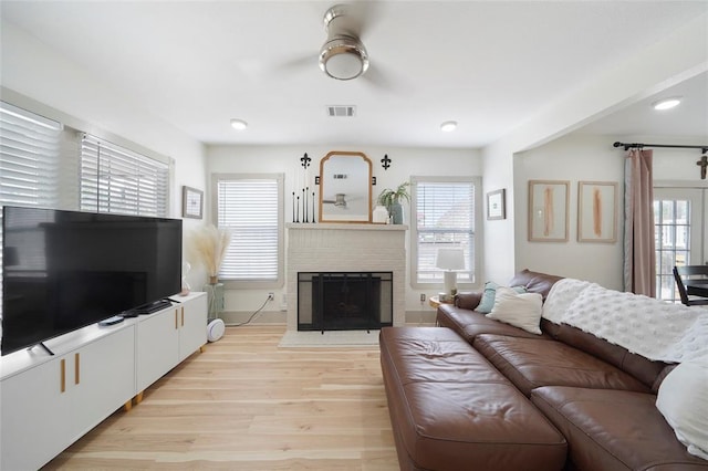 living room featuring light wood finished floors, a fireplace, and visible vents