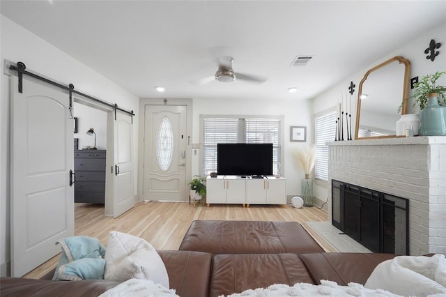 living area featuring a barn door, visible vents, ceiling fan, light wood-style floors, and a fireplace