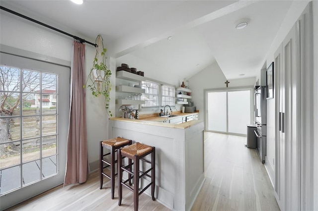 kitchen featuring a breakfast bar area, a peninsula, wooden counters, open shelves, and light wood finished floors