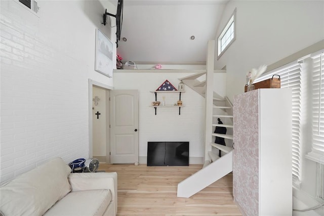 living room with visible vents, light wood-style flooring, a towering ceiling, brick wall, and stairs