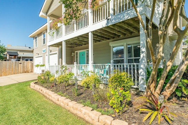 exterior space featuring a porch, a garage, fence, driveway, and a lawn