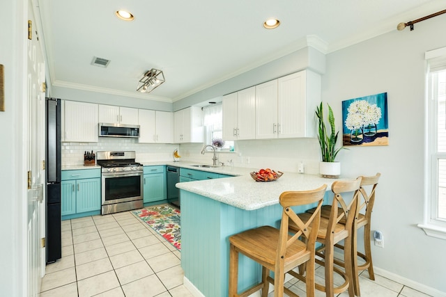 kitchen featuring a peninsula, a sink, visible vents, ornamental molding, and appliances with stainless steel finishes