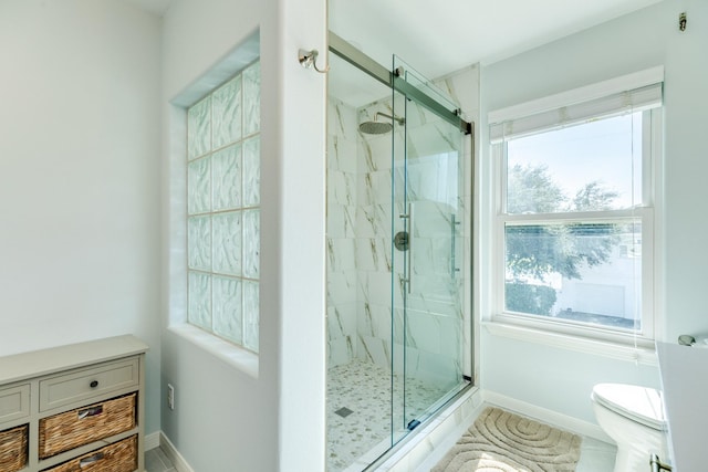 bathroom with baseboards, toilet, and a marble finish shower