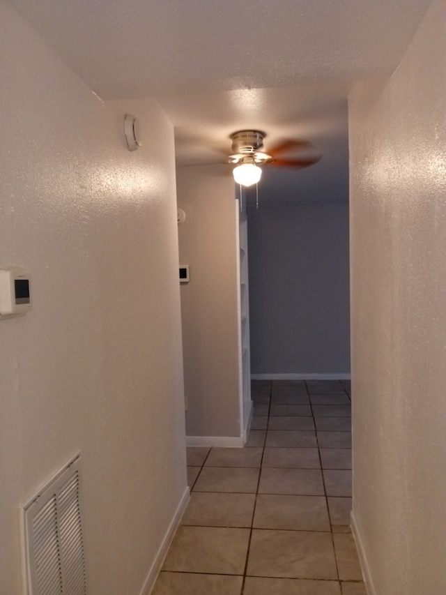 hall featuring light tile patterned floors, visible vents, and baseboards