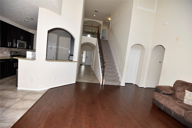 living room featuring stairs, a high ceiling, arched walkways, and light wood-style floors