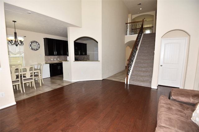 living area with a notable chandelier, wood finished floors, a towering ceiling, baseboards, and stairs