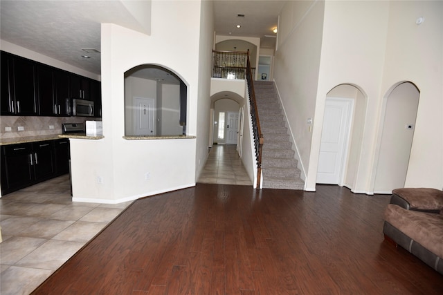 interior space featuring dark cabinets, stainless steel appliances, a high ceiling, open floor plan, and light wood-type flooring