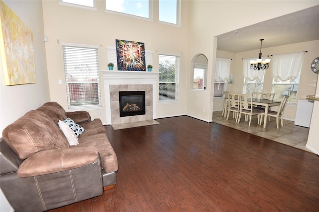 living room with a tile fireplace, a high ceiling, baseboards, dark wood finished floors, and an inviting chandelier