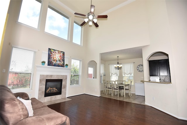 living area featuring ceiling fan with notable chandelier, a fireplace, wood finished floors, and baseboards