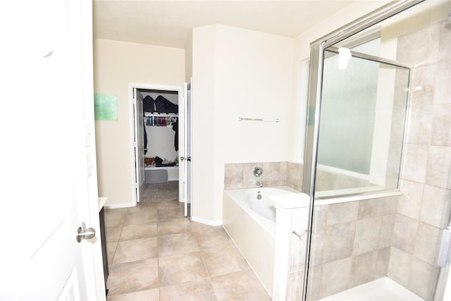 bathroom featuring a walk in closet, a shower stall, tile patterned flooring, baseboards, and a bath