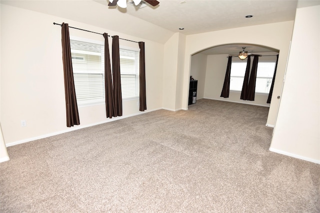 unfurnished room featuring arched walkways, ceiling fan, lofted ceiling, light colored carpet, and baseboards