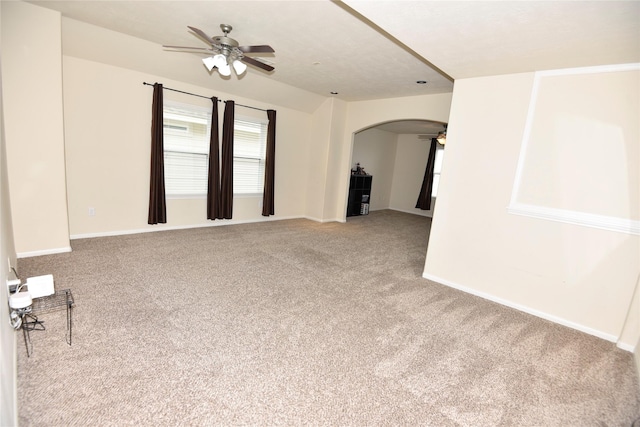 unfurnished room featuring a ceiling fan, arched walkways, light colored carpet, and baseboards