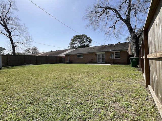 rear view of property featuring french doors, a fenced backyard, a yard, and brick siding