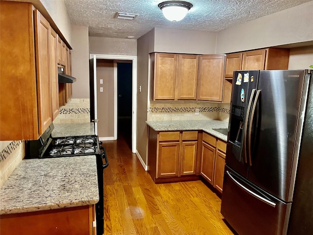 kitchen featuring brown cabinets, light wood finished floors, visible vents, black refrigerator with ice dispenser, and gas range