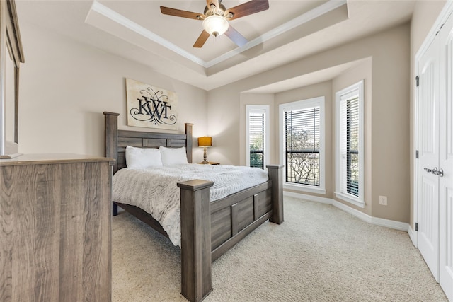 bedroom featuring baseboards, a ceiling fan, light colored carpet, a tray ceiling, and crown molding