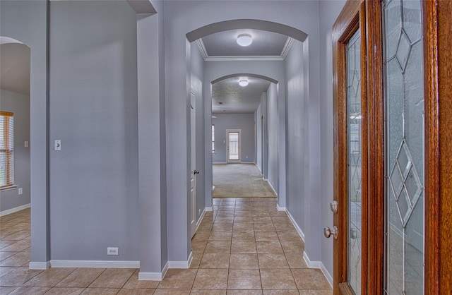 corridor featuring arched walkways, ornamental molding, light tile patterned flooring, and baseboards