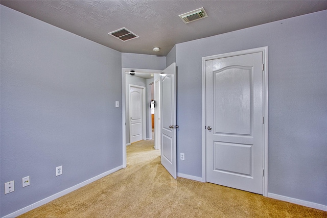 unfurnished bedroom featuring baseboards, a textured ceiling, visible vents, and light colored carpet