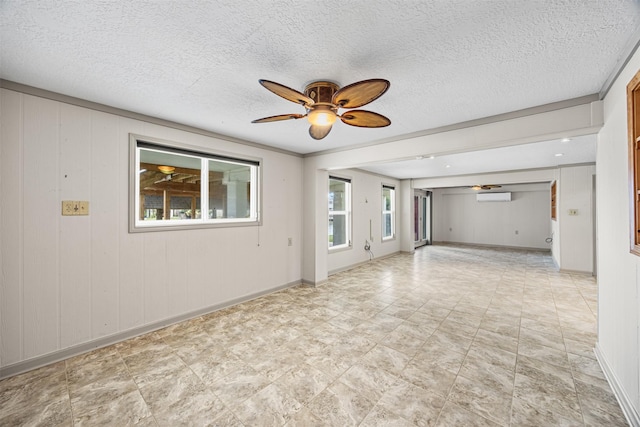 empty room with baseboards, a textured ceiling, a wall mounted AC, and ceiling fan