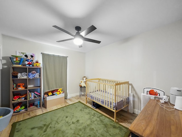 bedroom featuring ceiling fan, baseboards, a crib, and wood finished floors