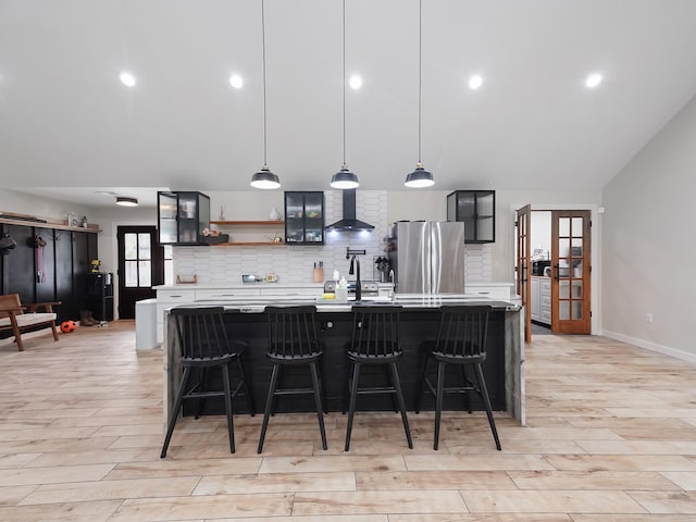 kitchen featuring wall chimney range hood, backsplash, light countertops, and freestanding refrigerator