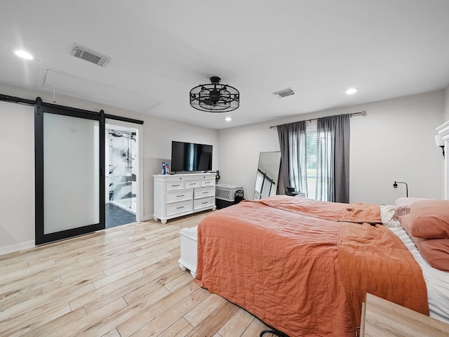 bedroom featuring visible vents, recessed lighting, light wood-style floors, and a barn door