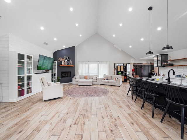 living area with light wood-type flooring, high vaulted ceiling, visible vents, and a fireplace