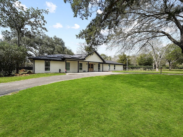 view of front of property with roof mounted solar panels, driveway, and a front lawn