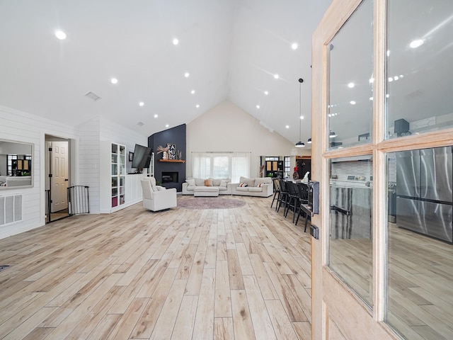 living room featuring visible vents, a fireplace, high vaulted ceiling, and wood finished floors