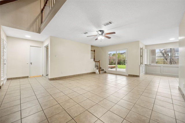 unfurnished living room with ceiling fan, visible vents, light tile patterned flooring, and stairs