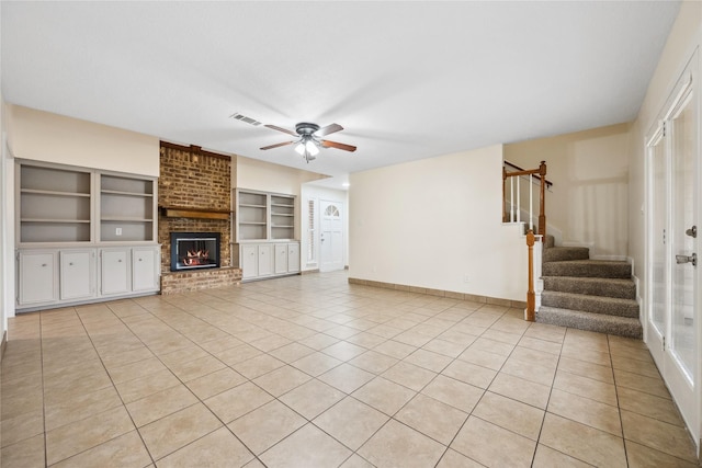 unfurnished living room with light tile patterned floors, visible vents, a brick fireplace, and stairs