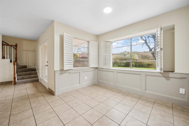 unfurnished room featuring light tile patterned floors, stairway, and a decorative wall