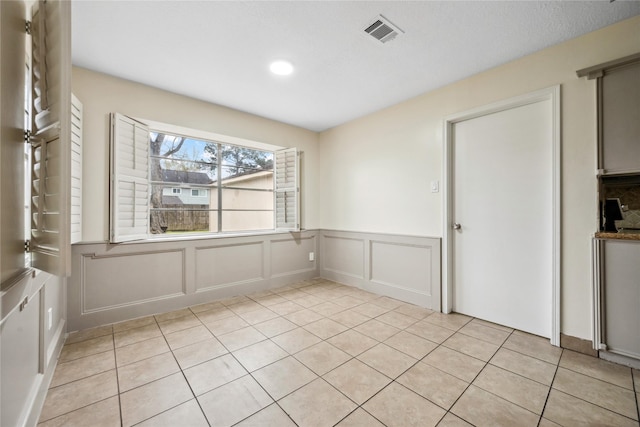 unfurnished dining area featuring a wainscoted wall, a decorative wall, light tile patterned floors, and visible vents