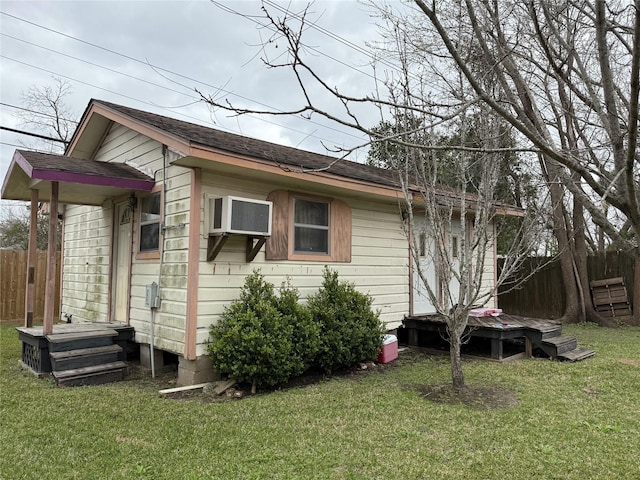 view of home's exterior featuring a yard, an AC wall unit, a shingled roof, and fence