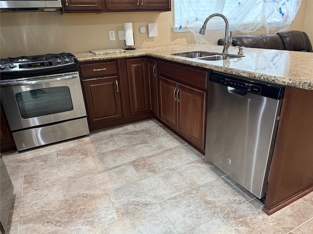 kitchen with light stone counters, stainless steel appliances, a sink, dark brown cabinets, and extractor fan