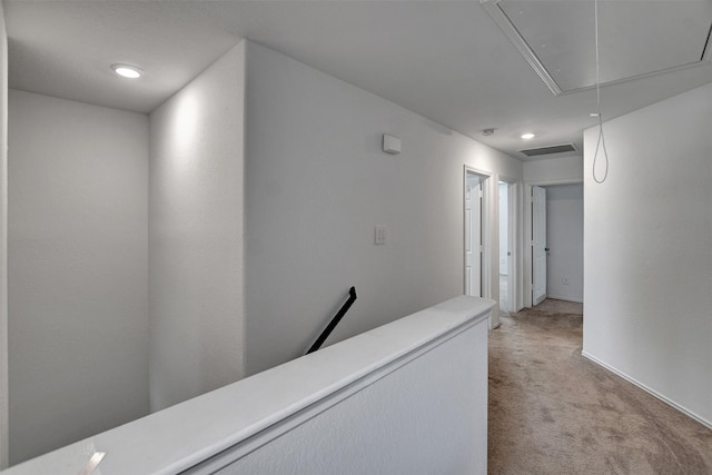 hall with visible vents, an upstairs landing, attic access, and light colored carpet