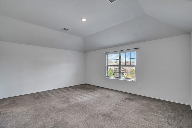 spare room with vaulted ceiling, dark carpet, and visible vents