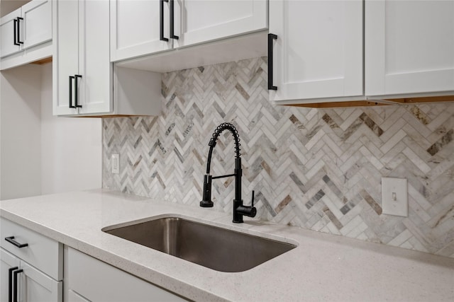 kitchen with tasteful backsplash, white cabinetry, a sink, and light stone counters