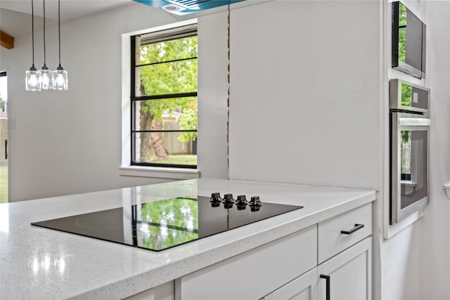 kitchen with black electric stovetop, hanging light fixtures, white cabinets, light stone countertops, and oven