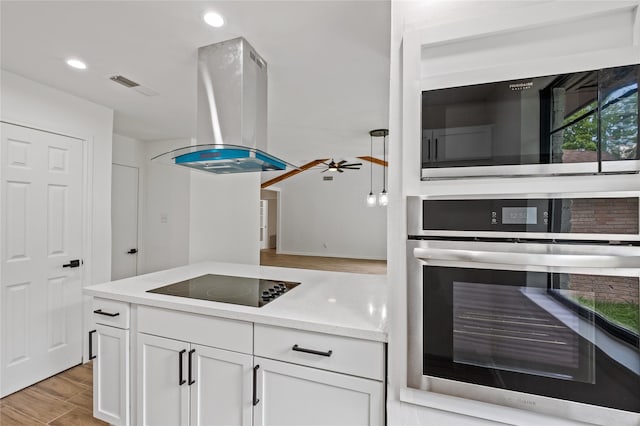 kitchen with oven, black electric cooktop, white cabinetry, light wood finished floors, and island exhaust hood