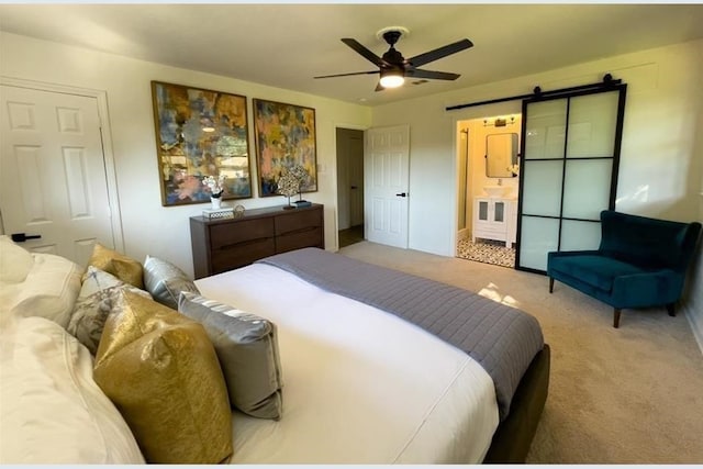 bedroom featuring light carpet, a barn door, ceiling fan, and ensuite bathroom