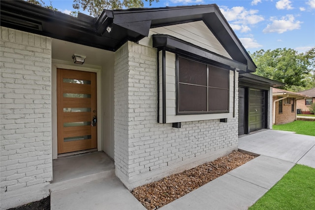 view of exterior entry with an attached garage, driveway, and brick siding