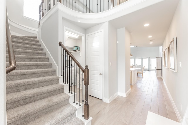 stairway featuring a towering ceiling, baseboards, wood finished floors, and recessed lighting