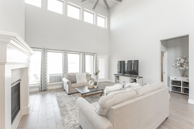 living room featuring a ceiling fan, a brick fireplace, and light wood finished floors