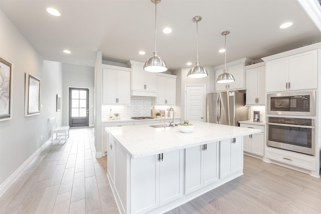 kitchen with a center island with sink, stainless steel appliances, tasteful backsplash, light wood-style flooring, and a sink