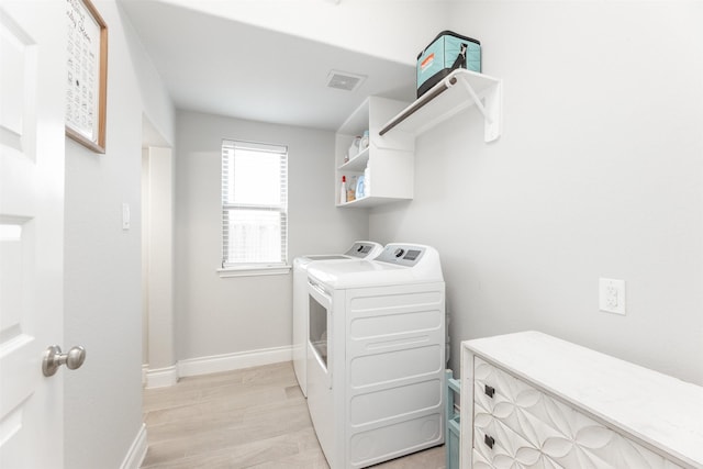 laundry area with washing machine and clothes dryer, visible vents, light wood-type flooring, laundry area, and baseboards