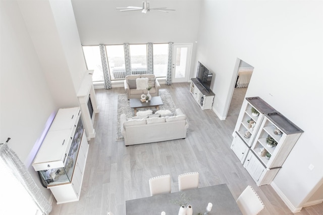 living room with baseboards, light wood-type flooring, a towering ceiling, and a ceiling fan