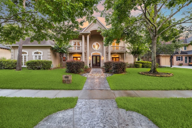 greek revival house with a yard, stucco siding, and french doors