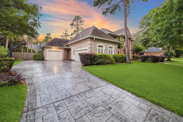 view of front of property featuring decorative driveway, stucco siding, a front yard, fence, and a garage